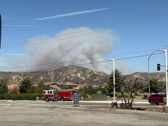 On Thursday, August 7th, 2025, at 7:30am, multiple fire crews responded to a fire near Holser Canyon Road, north of Piru. Later named the Canyon Fire, residents were able to see plumes of smoke fill the air as they watched crews head towards the fire. Above is a photo taken from the Arco Gas Station off Highway 126 in Piru. Photo credit Marcus Camp. Inset, a helicopter making a water drop. They can drop 1,000 gallons (about 3,785 liters) of water at once, some much more, and can be the best way to attack fires that are difficult for ground crews to reach. Photo credit Sebastian Ramirez.