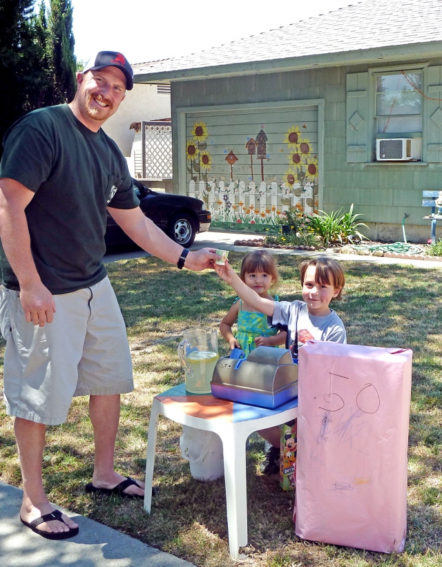 Dylan Dunst, 5, hands a glass of cold lemonade to his dad, Scott, while friend Maddie, 2 1/2, looks on. Dylan was manning his own lemonade stand last week to raise money for a trip to Disneyland. He made $8.50.