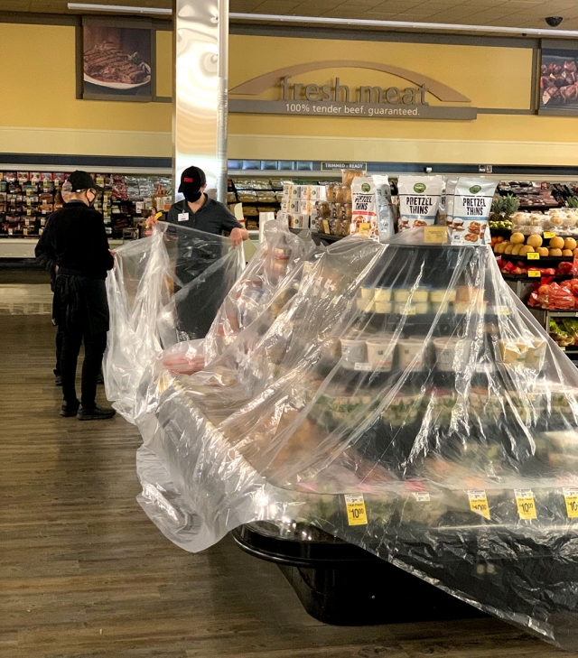 Store employees covering the refrigerated and freezer sections with plastic.